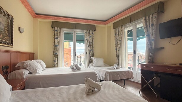 Une chambre d’hôtel avec deux lits, une télévision, un bureau et un balcon avec des rideaux.