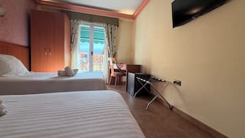 Habitación de hotel con dos camas, un escritorio, una silla, un televisor y vistas a edificios a través de una ventana.