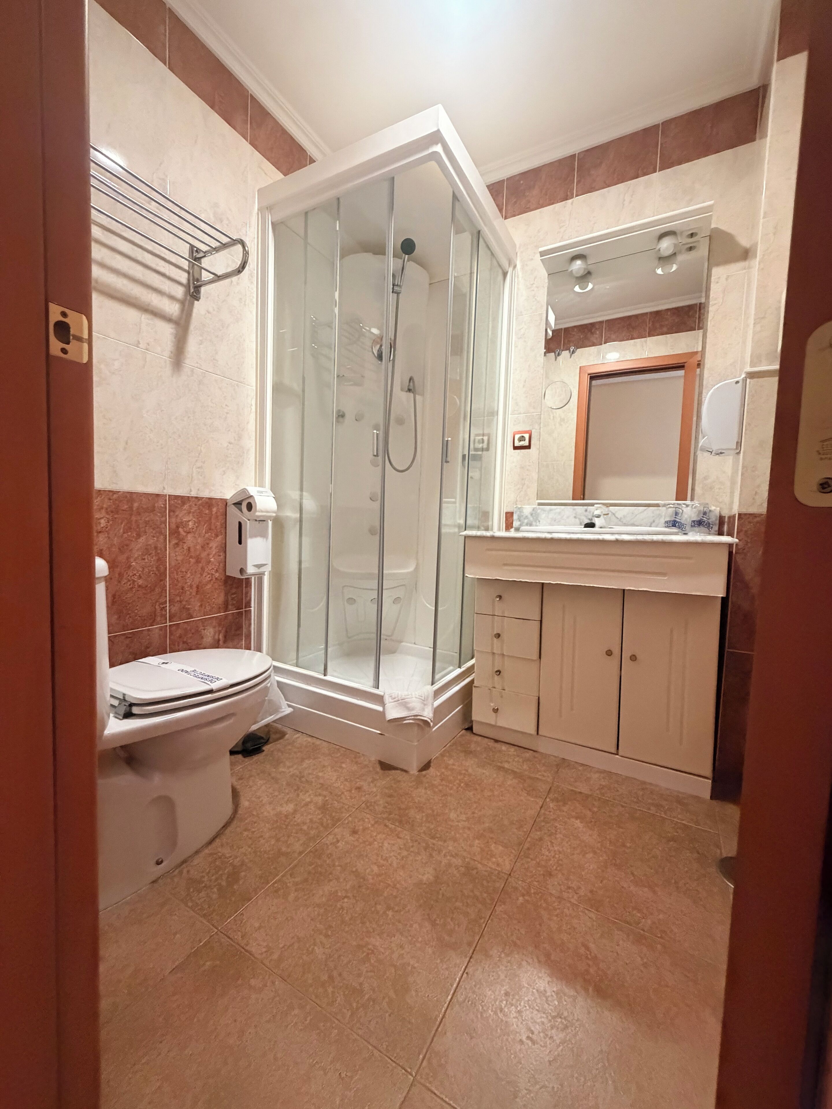 Ein Badezimmer mit Duschkabine, Toilette, Waschbecken inklusive Spiegel und Handtuchhalter.