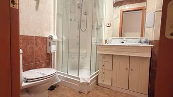 Ein Badezimmer mit Duschkabine, Toilette, Waschbecken inklusive Spiegel und Handtuchhalter.