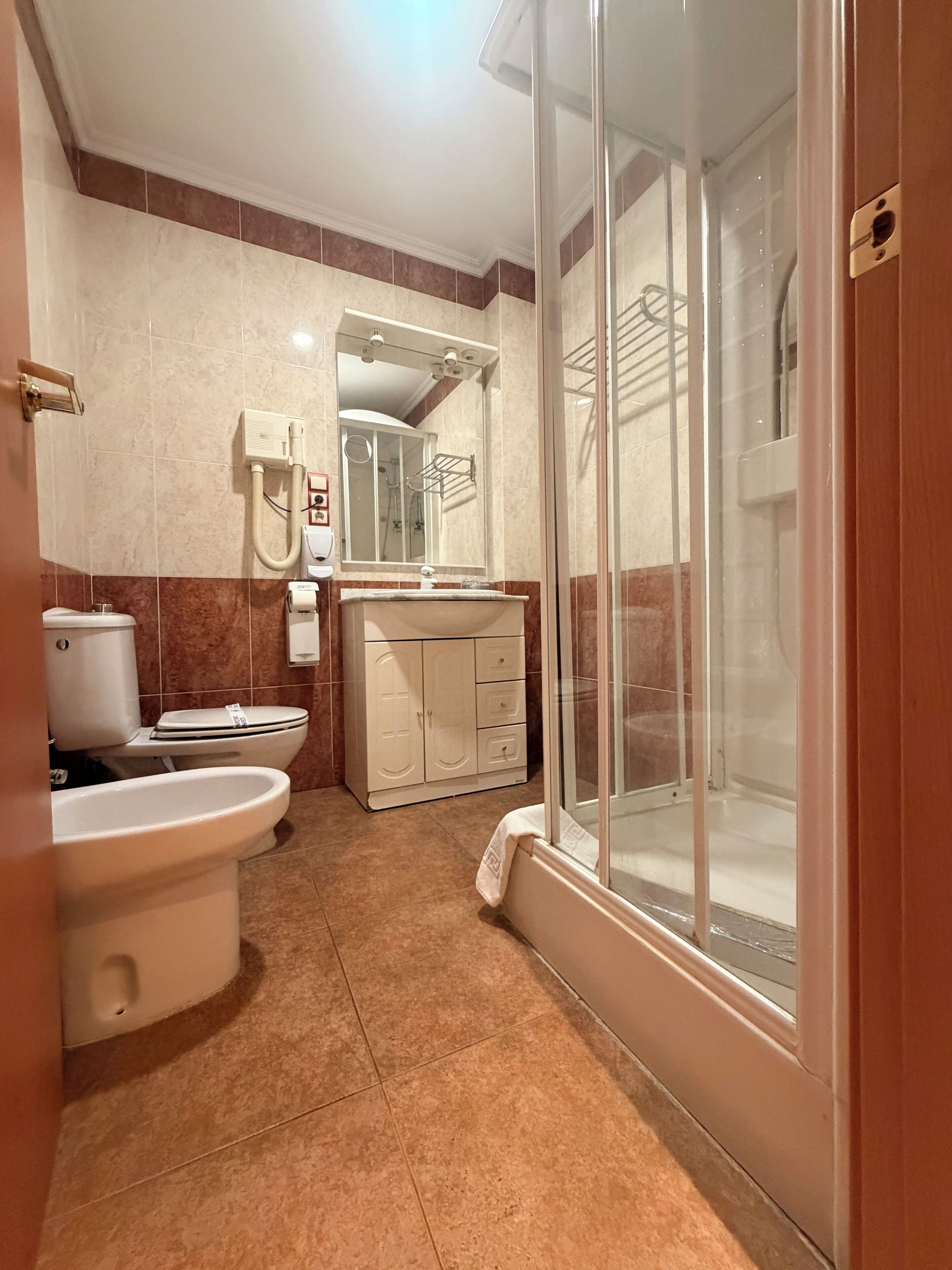 Un baño con inodoro, bidé, lavamanos y ducha con mampara de vidrio.