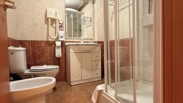 Un baño con inodoro, bidé, lavamanos y ducha con mampara de vidrio.