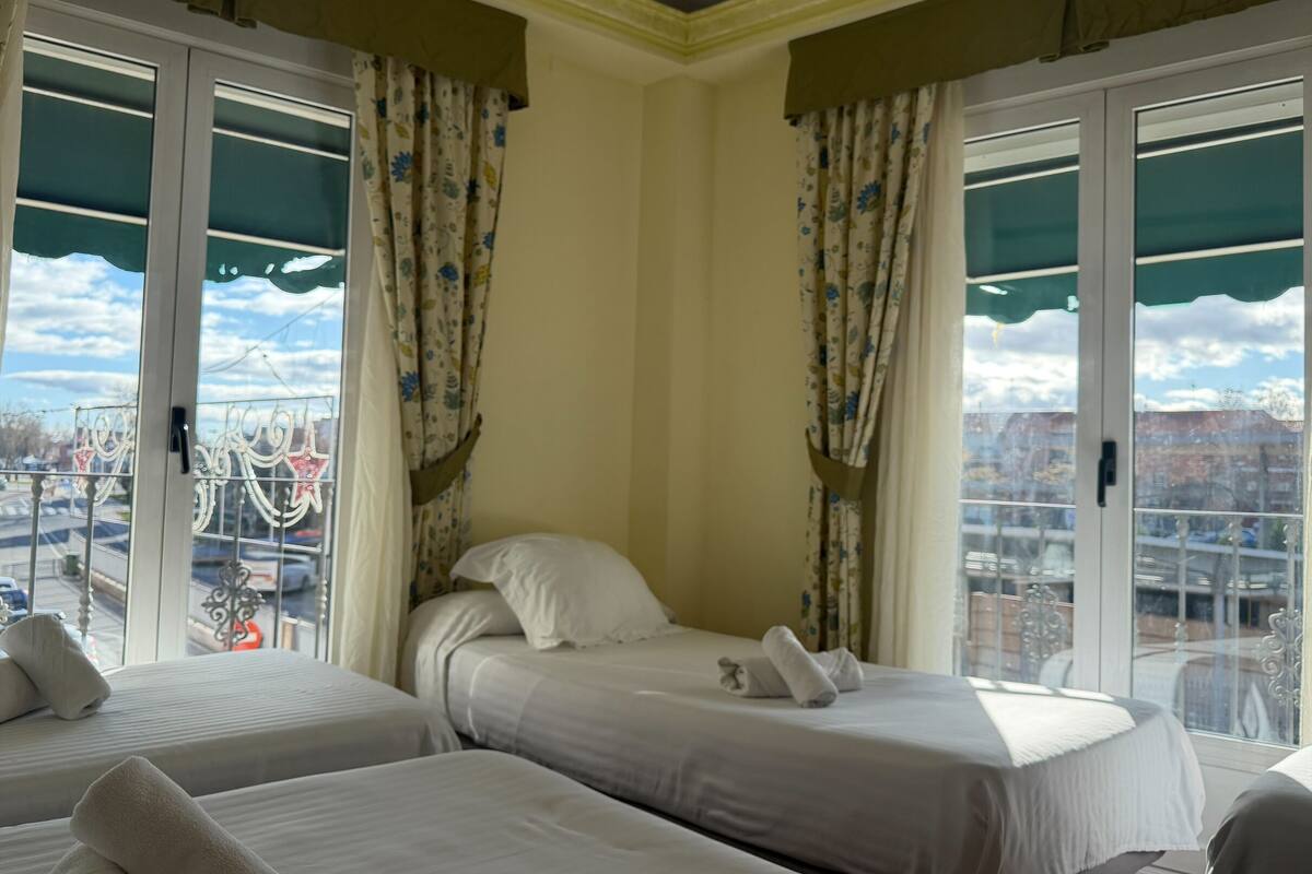 Een hotelkamer met twee bedden, bloemen gordijnen en uitzicht op de stad.