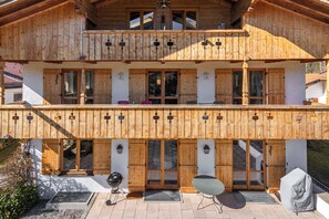 A wooden chalet with a balcony, a barbecue grill, and a covered outdoor seating area.