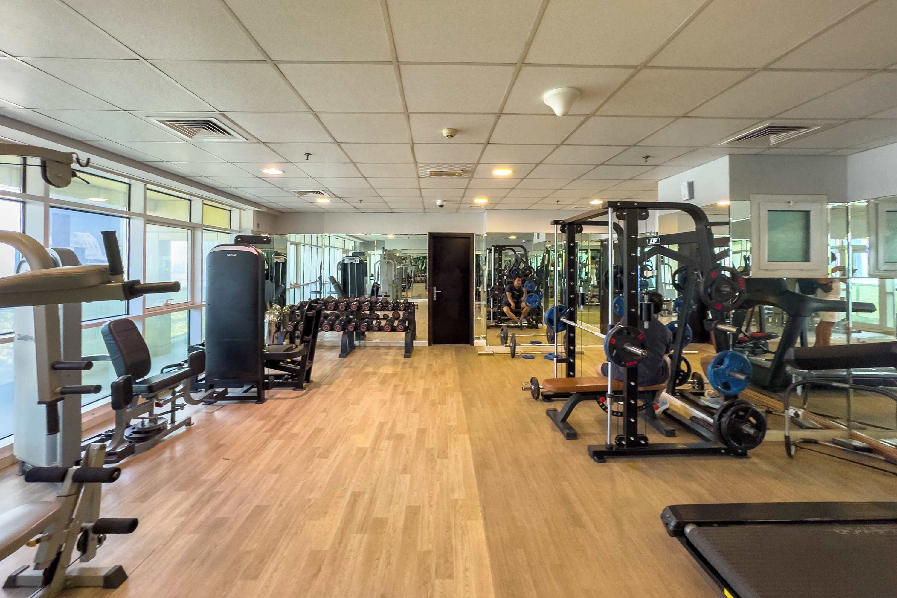 A gym with various exercise equipment, large windows, and a wooden floor.