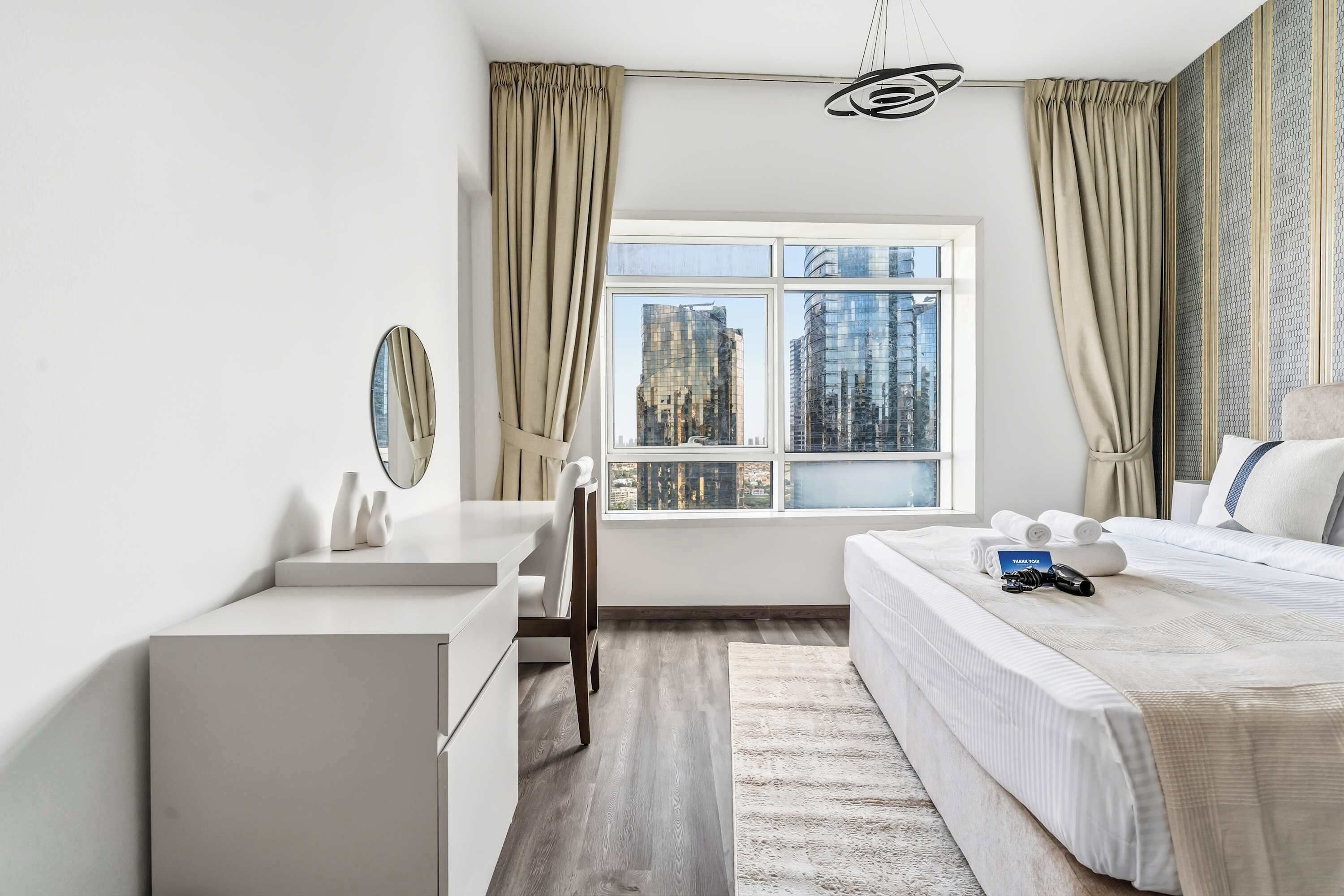 Moderni hotellihuone, jossa on suuri sänky, työpöytä ja näkymä korkeisiin rakennuksiin.