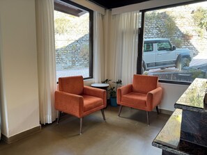 A room with two orange armchairs, a small round table, and a potted plant. - Manali Se - Your Home in the Pines (Jagatsukh)