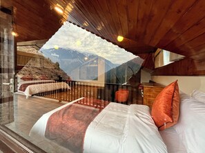 A bedroom with a bed, pillows, a wooden ceiling, and a mountain view through a window. - Manali Se - Your Home in the Pines (Jagatsukh)