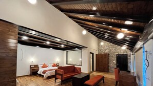 A modern interior with a wooden floor, a sofa, a bed with pillows, a stone wall, and a large mirror. - Manali Se - Your Home in the Pines (Jagatsukh)