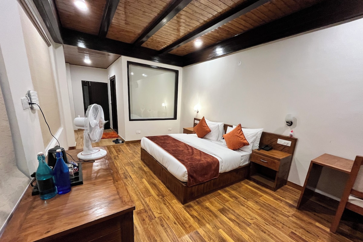 A hotel room with a wooden floor, a bed with white bedding and brown pillows, a bedside table with a phone, and a nightstand.