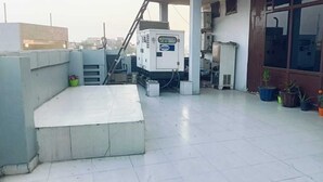 A rooftop terrace with a concrete bench, industrial equipment, and potted plants. - The PFNL Residency (Gohana)