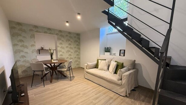 A living room with a sofa, a dining table with chairs, a staircase, and a wall with a 'HOME' sign. - Riviera Collection - Dream Lofts in the Heart of Naples (Napoli)