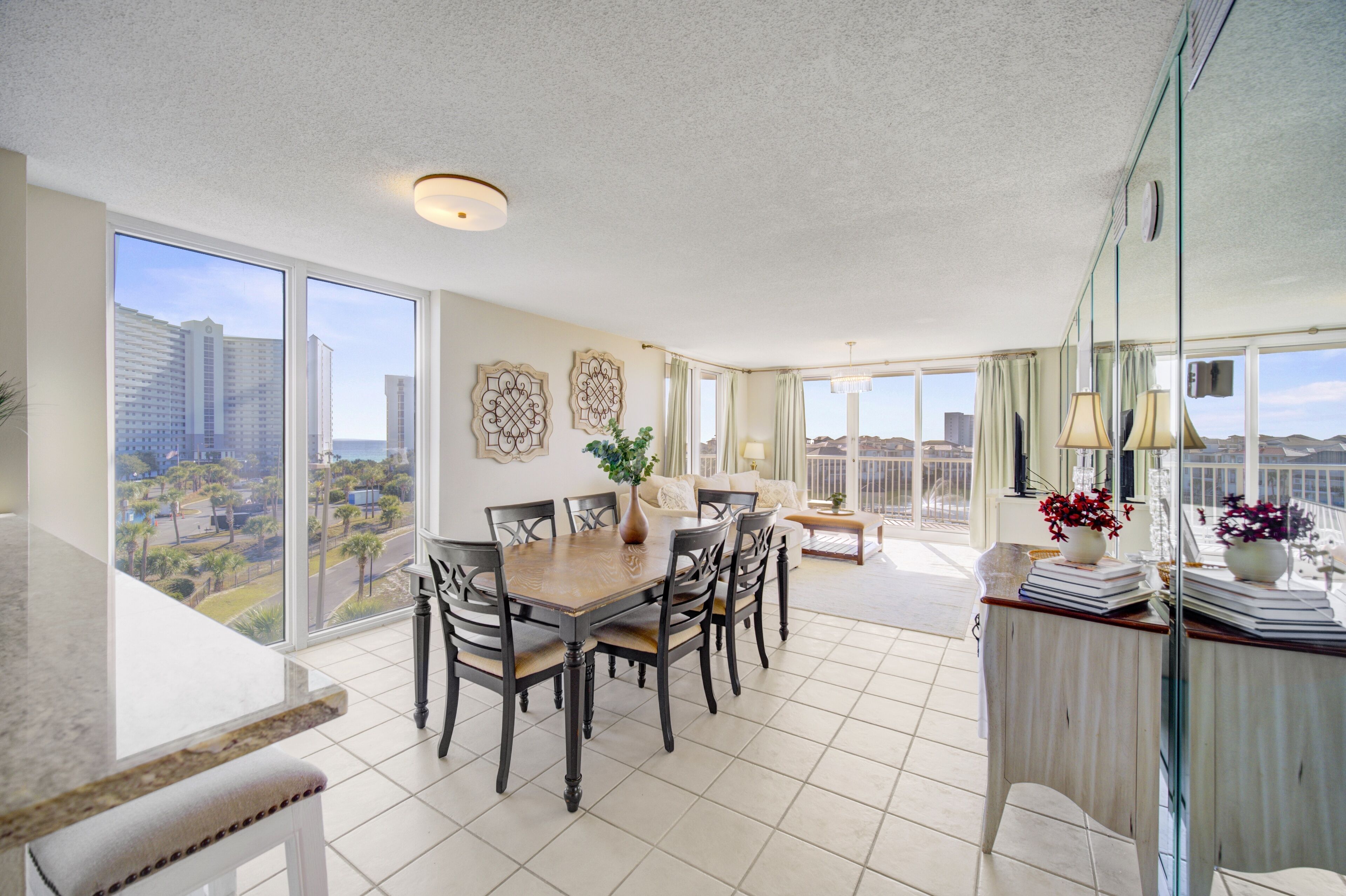 A spacious dining area with a large table and chairs, a vase with flowers, and a view of the city through large windows.