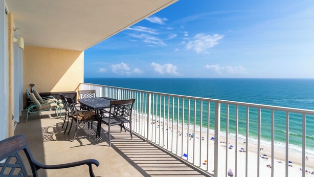 Ein Balkon mit Blick auf den Ozean und den Strand, ausgestattet mit Stühlen und einem Tisch.