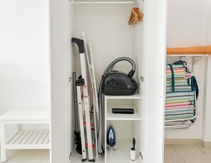 A closet with a vacuum cleaner, ironing board, and a striped bag. - BnB Homes vibrant Ocean View terraced apartment with swimming pool 200m to beach (Armação de Pêra)