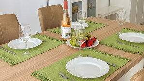 A dining table set with plates, glasses, and a bottle of wine, with a coffee machine and cabinets in the background.