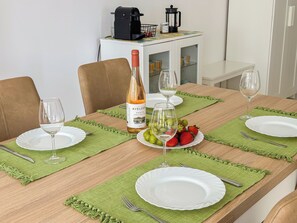 A dining table set with plates, glasses, and a bottle of wine, with a coffee machine and cabinets in the background. - BnB Homes vibrant Ocean View terraced apartment with swimming pool 200m to beach (Armação de Pêra)