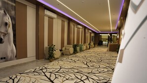 A hotel corridor with a patterned carpet, seating area with chairs and plants, and a large horse statue. - Nouf plaza (Al Duwadimi)