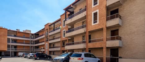 Un edificio residencial de varios pisos con balcones, coches aparcados y cielo despejado.