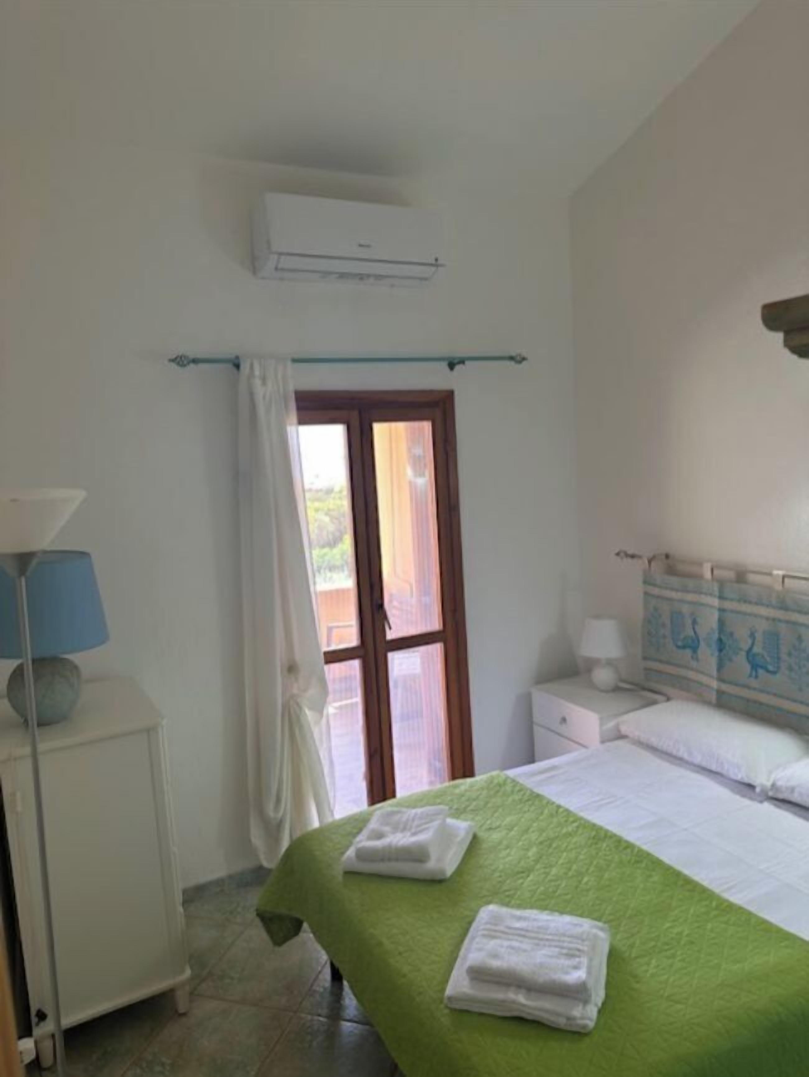 Une chambre d’hôtel équipée d’un lit, d’une table de chevet, d’une lampe, d’un climatiseur et d’une fenêtre avec des rideaux.