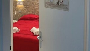 Ein Zimmer mit einer Steinwand, einem Bett mit roter Bettdecke und einem an der Wand befestigten Kunstwerk aus Muscheln.