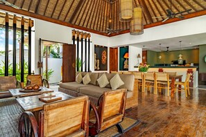 A spacious living area with a wooden ceiling, a sofa set, a dining table with chairs, and a kitchen area in the background. - Villa Abagram Seminyak (Seminyak)