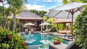 A pool area with lounge chairs and umbrellas, surrounded by lush greenery. - Villa Abagram Seminyak (Seminyak)