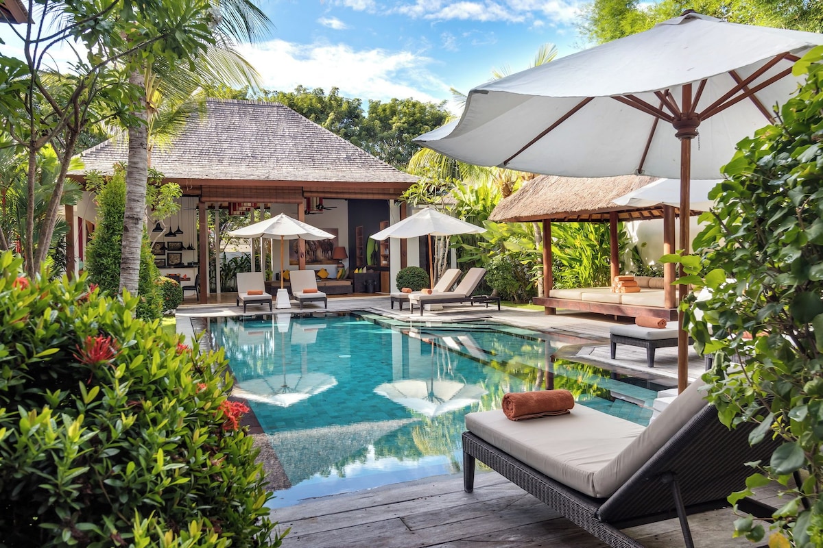 A pool area with lounge chairs and umbrellas, surrounded by lush greenery.