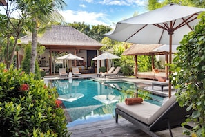 A pool area with lounge chairs and umbrellas, surrounded by lush greenery. - Villa Abagram Seminyak (Seminyak)