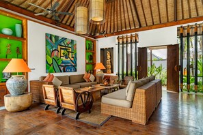 A spacious living area with a high ceiling, wooden flooring, and a large painting. There are two sofas, a coffee table, and a lamp. - Villa Abagram Seminyak (Seminyak)