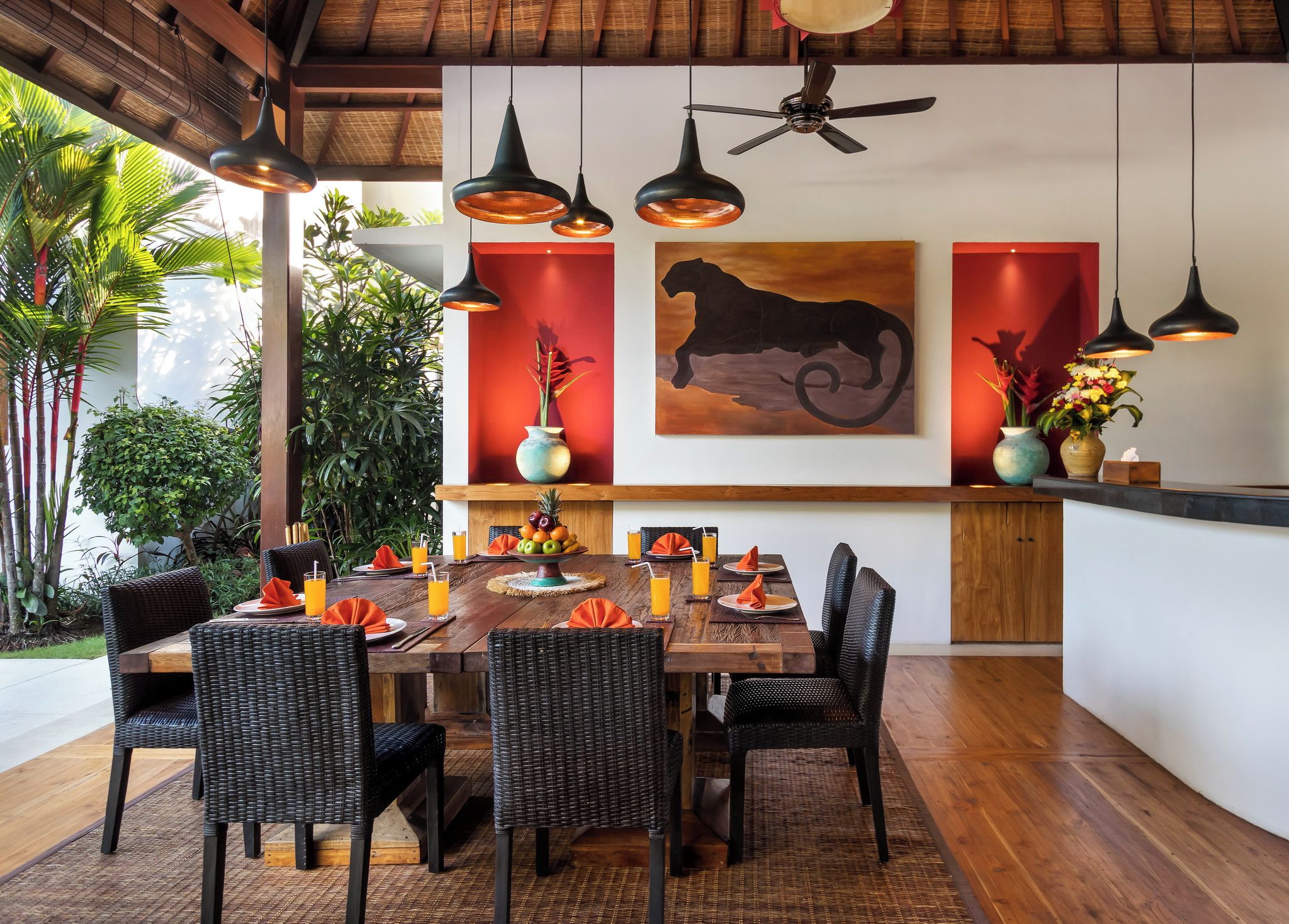 Un comedor al aire libre con una mesa de madera, sillas de mimbre e iluminación colgante.