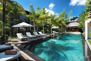 A pool area with lounge chairs and umbrellas, surrounded by palm trees and a clear blue sky. - Villa Abagram Seminyak (Seminyak)