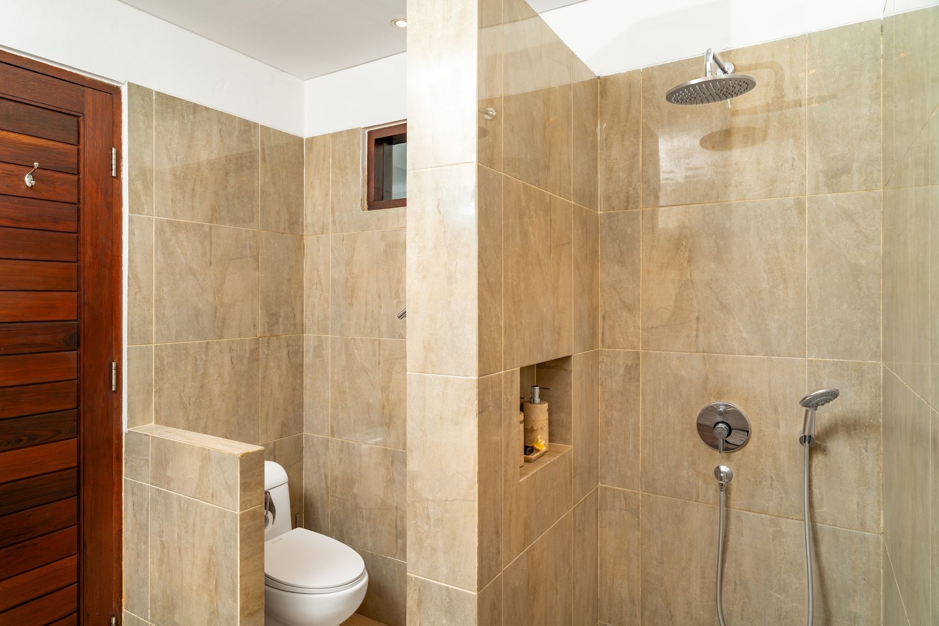 Une salle de bain comprenant des toilettes, une douche avec un pommeau de douche amovible et un robinet mural.