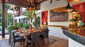 Un coin repas avec une table en bois dressée pour six personnes, entourée de chaises en osier, sous un ventilateur de plafond.