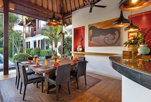 A dining area with a wooden table set for six, surrounded by wicker chairs, under a ceiling fan. - Villa Abagram Seminyak (Seminyak)