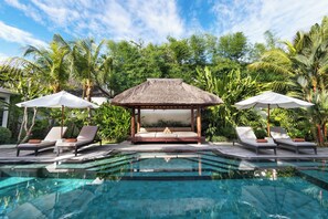 A poolside area with lounge chairs, a thatched gazebo, and lush tropical vegetation. - Villa Abagram Seminyak (Seminyak)