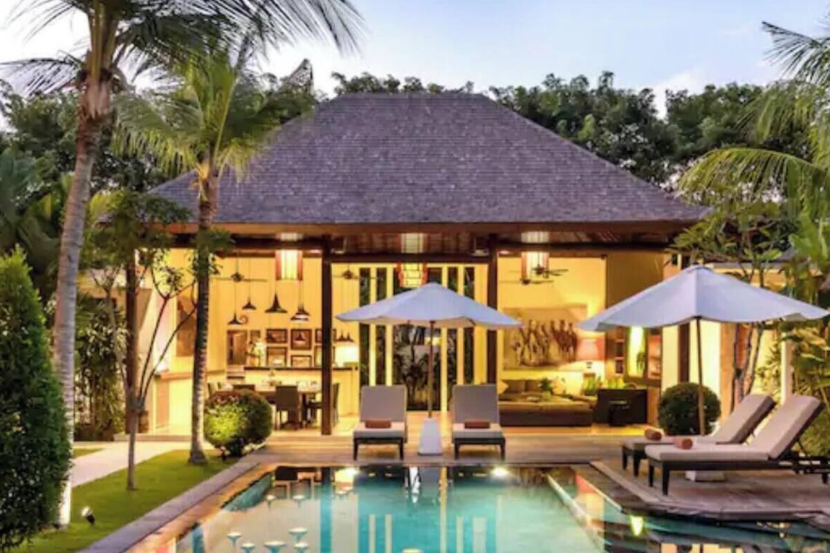 A poolside area with lounge chairs and umbrellas, a pool, and a building with a tiled roof.