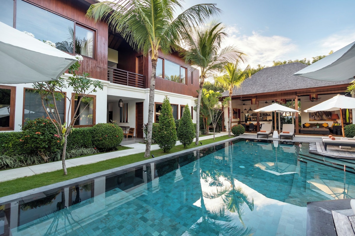 A modern pool area with a clear pool, lounge chairs, and umbrellas.