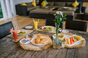 A dining table set with plates of food, a drink, and a vase with flowers. - Villa Abagram Seminyak (Seminyak)