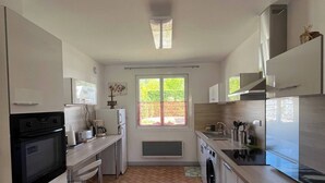 A modern kitchen with a herringbone floor pattern, stainless steel appliances, and a large window providing natural light. - Les Mésanges Bleues (Le Poët-Laval)