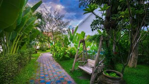 Un camí de jardí amb un bressol, una cadira de fusta i una olla gran.