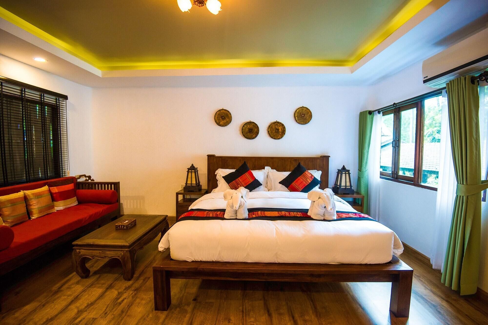 Habitación de hotel con una cama de madera, un sofá rojo, una mesa de centro de madera y una ventana con cortinas verdes.