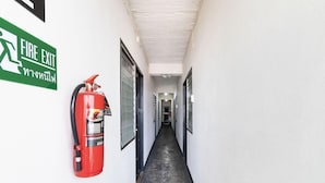A hallway with a fire exit sign and a fire extinguisher mounted on the wall. - Baan Lanna At Phrasingh (Chiang Mai)