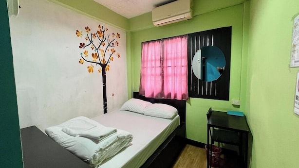 A small, single-bed room with a tree mural, a round mirror, and a window with pink curtains. - Baan Lanna At Phrasingh (Chiang Mai)