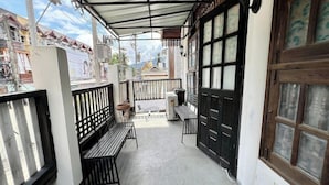 A covered outdoor seating area with benches, a trash bin, and a door with glass panels. - Baan Lanna At Phrasingh (Chiang Mai)