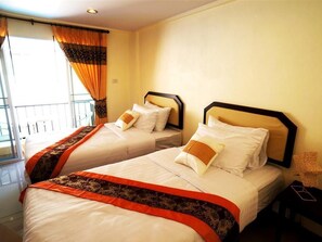 Two twin beds with matching headboards and decorative pillows, a window with curtains, and a small table with a lamp. - Manee Guest House (Chiang Mai)