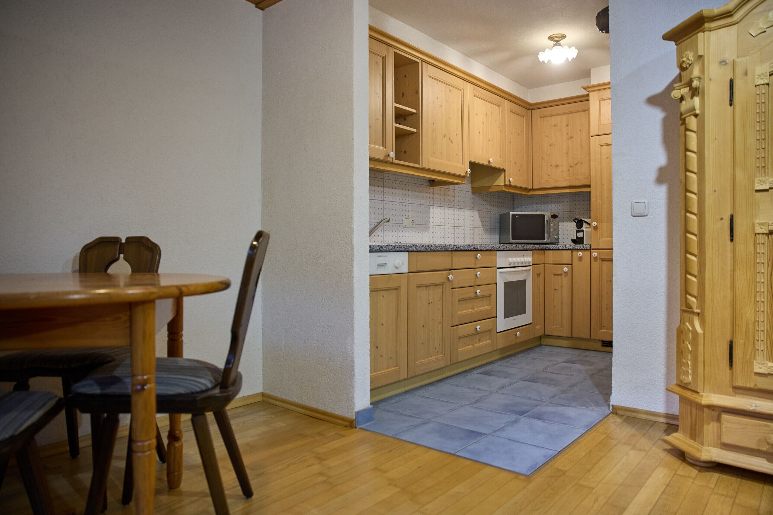 A kitchen with wooden cabinets, a microwave, an oven, and a dining table with chairs.