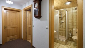 A hallway with wooden doors, a wall-mounted clock, and a shower room with a glass door. - 1316 Alt Montafon Apartment 16 (Gaschurn)