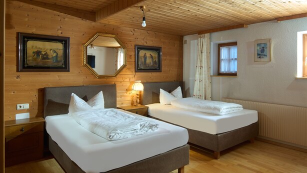 A hotel room with two beds, wooden walls, a mirror, and framed pictures. - 1316 Alt Montafon Apartment 16 (Gaschurn)