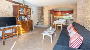 Un salon comprenant un canapé, un téléviseur, un meuble en bois et un coin repas avec une table et des chaises.